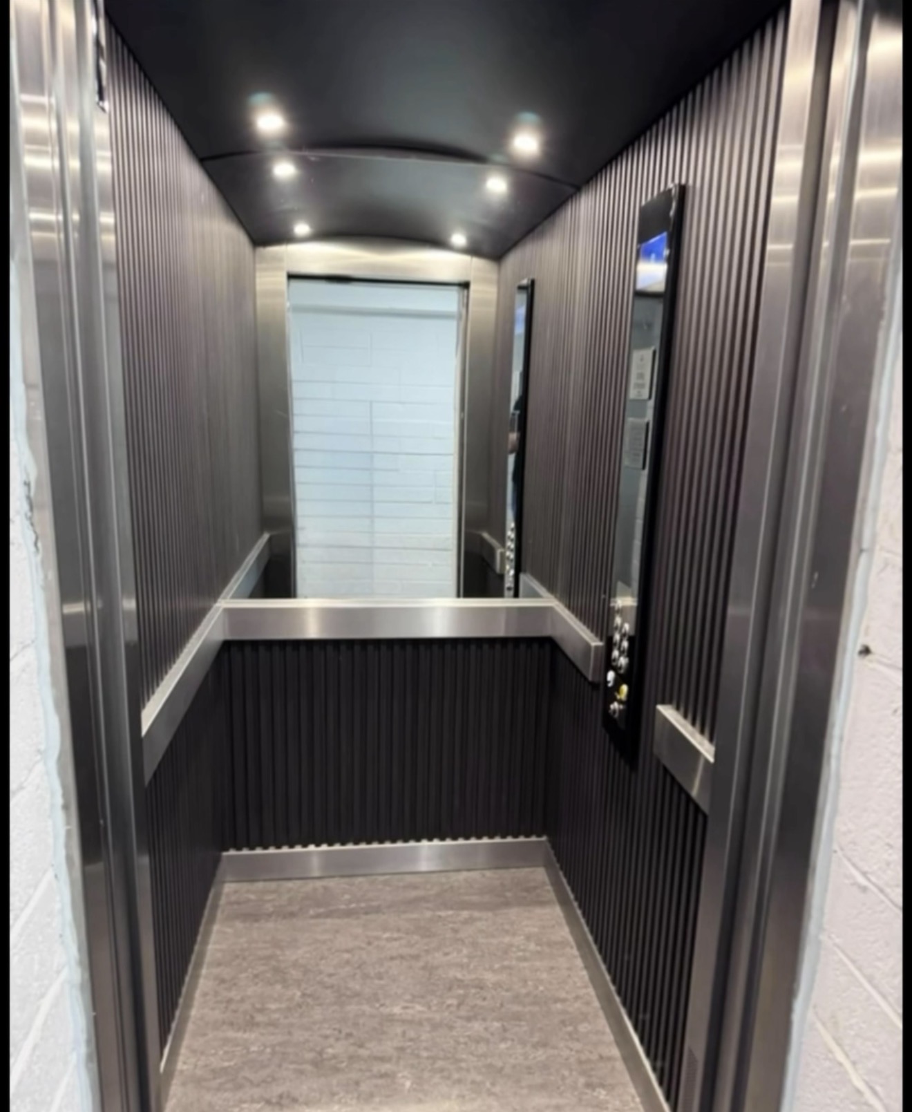 Lift interior with dark wall panels, mirror, handrails and ceiling spotlights